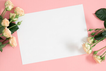 Blank white paper, bouquet of light beautiful cream roses on pastel pink background. Festive flower composition. Top view, flat lay.