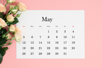 Flat lay of May 2024 paper desk calendar, top view. White beautiful roses on a pastel pink background.