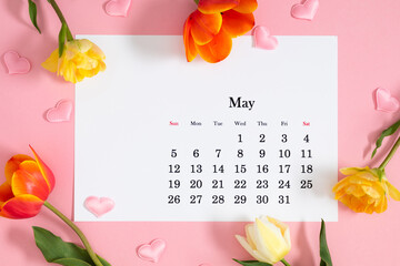 Flat lay of May 2024 paper desk calendar, top view. A bouquet of bright multi-colored tulips on a pastel pink background.