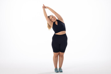 Caucasian plus-size model in sportswear stretches on a white background