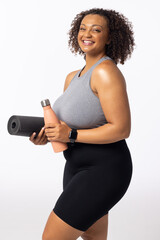 Biracial plus size model with yoga mat and water bottle, smiling, white background - 792789616