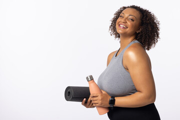A biracial young female plus size model holds yoga mat and water bottle, copy space - 792789620
