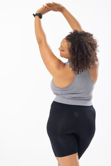 Biracial plus size model stretches arms up, in sports gear on white background