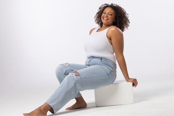 Biracial plus size model sits smiling on white background, copy space