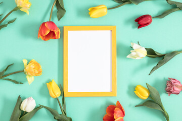 Festive floral background. Beautiful tulip flowers and yellow empty photo frame on a pastel mint background. Top view, flat lay.