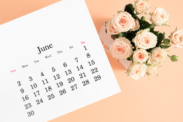 Flat lay of June 2024 paper desk calendar, top view. White beautiful roses on a light beige...
