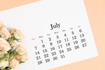 Flat lay of paper desk calendar for July 2024, top view. White beautiful roses on a light beige...