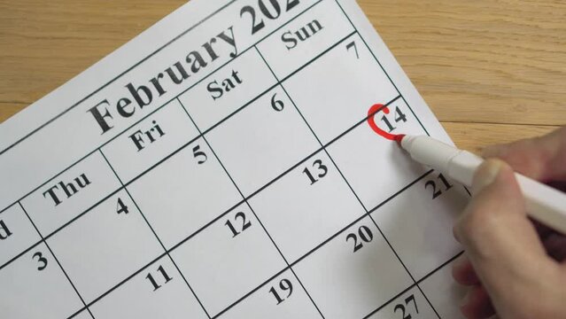 Male hand drawing a red heart shape around 14 February in calendar. Valentine's day.