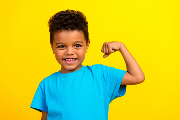 Portrait of strong cheerful schoolboy with afro hair wear blue t-shirt show biceps clenching fist...