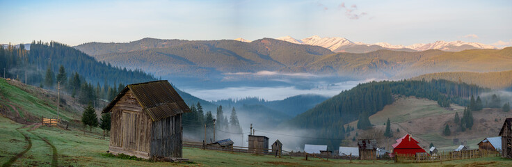 View of mountain village surrounded by peaks of Carpatian mountains with wooden cabins and faint...