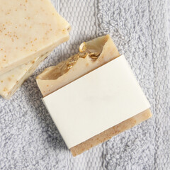 Beige handmade soap bar with blank label on light grey folded towel top view, mockup