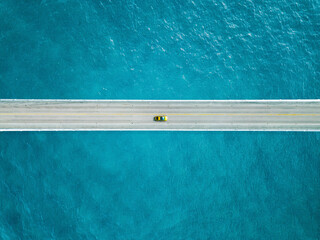 Aerial view of bridge road with yellow car over blue sea ocean