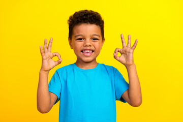 Photo of good mood adorable child with curly hair dressed blue t-shirt showing okey nice job...