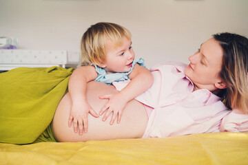 Pregnant mother and daughter together at home. Woman with her first child during second pregnancy. Motherhood and parenting concept. Toddler smiling girl and mom. Happy family expecting for new baby. - 792807410