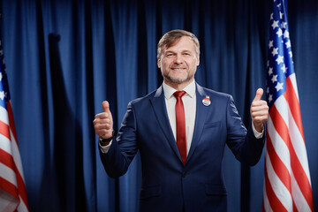 Successful mature male politician in formalwear showing thumbs up and looking at camera with smile...
