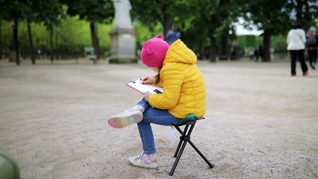 Young preschooler painter drawing outdoor scene with fusain in Luxembourg garden of Paris, France.