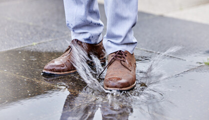 Person, puddle and shoe stepping in water on ground for commute to work, job or business. Splash,...
