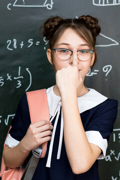 A beautiful schoolgirl adjusts her glasses her nose while standing at the school board.