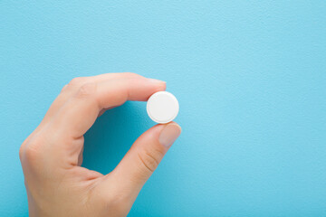 Young adult woman hand fingers holding and showing white pill of c vitamin on light blue table background. Pastel color. Receiving nutrition supplement. Closeup. Top down view. - 792819430