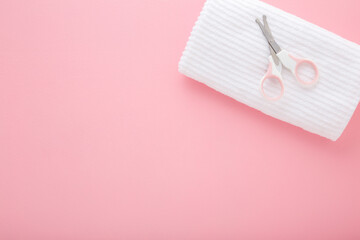 Scissors and white soft towel on light pink table background. Pastel color. Closeup. Baby nail cutting. Top down view.