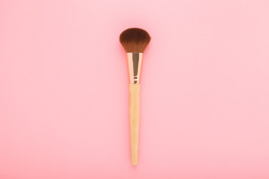 New big makeup brush with soft bristles on light pink table background. Pastel color. Female beauty product. Closeup. Top down view.