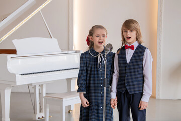 Two children are singing in front of a piano and a microphone.