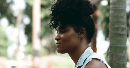 One contemplative young black woman profile close-up face in deep mental reflection sitting outside...