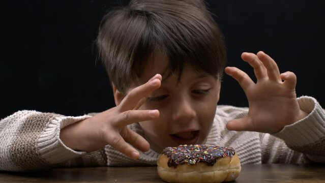Child wanting to eat donut on table, 5 year old boy anticipating sweet snack with open mouth awaiting sugar rush