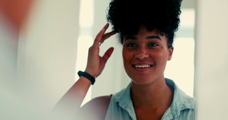 One joyful young black woman looking at herself in the mirror with confident gaze and sending a...