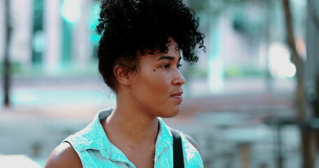 One pensive young black Brazilian woman standing outside gazing at park during sunny day in quiet...