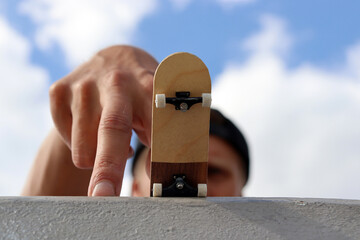 Hand playing with blank wooden fingerboard with a man in background waiting to drop down, close up....