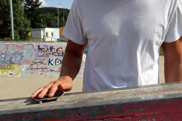 Male hand playing with black wooden fingerboard doing trick at the ramp in skatepark, close up. Mini skateboard, small skateboard deck © Tom