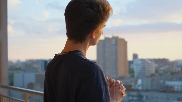An athlete stretching his neck on the balcony of a house at sunset, close-up