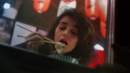girl eating noodles in a Chinese cafe with chopsticks. A woman in a restaurant is trying ramen soup