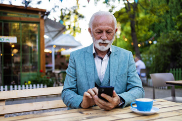 Mature guy is connected on a smartphone in the bar. Happy senior man using smartphone app while...