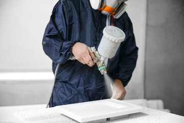 Application white color on facade kitchen furniture, spraying device. Painter staining wood with...