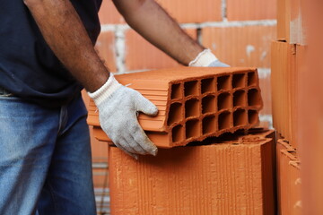 Construction worker lifting a brick. Builder working on construction site. Professional bricklayer...