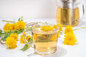 Dandelions plant herbal flower tea. Transparent glass cup and teapot with golden hot tea drink, on...