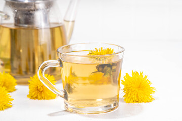Dandelions plant herbal flower tea. Transparent glass cup and teapot with golden hot tea drink, on white background with dandelion flowers and leaves