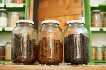 A trio of glass jars filled with assorted dried spices are neatly arranged on a wooden shelf, set...