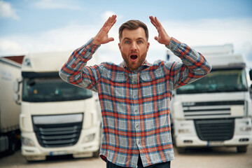 Shocked, scared, with hands up. Man is standing against trucks outdoors