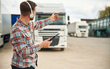 Showing the way, with tablet. Man is standing against trucks outdoors