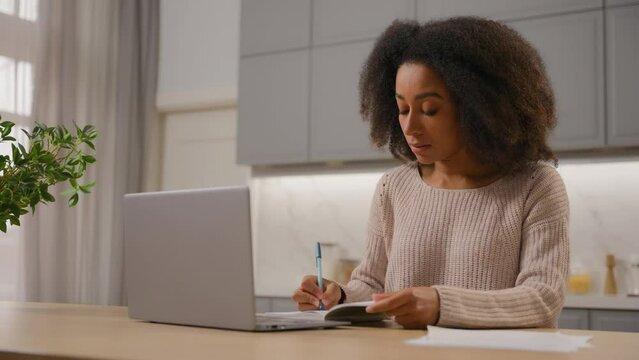 African American girl student ethnic woman studying with laptop at home working distant quarantine education female freelancer businesswoman writing notes in notebook on kitchen table computer work