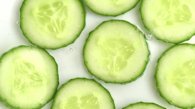 Cucumber slices in cucumber extract, gel texture. Top viewSlow motion of rotation ripe green sliced cucumbers in water, serum or gel.
