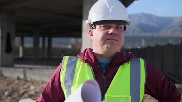 Tense foreman shaking his head dissatisfied with the result of a construction project standing near an unfinished building wearing a safety helmet, close up.