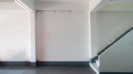 The image shows an empty room with white walls, a gray floor, and a staircase leading up to a...