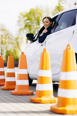 Woman sits in car , driving back and looking at the cones set up close to car