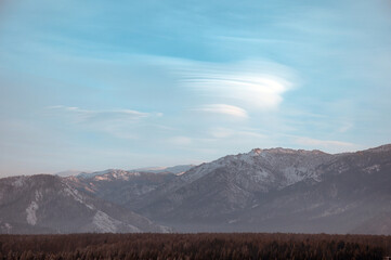 Cold snowy mountain landscape at sunset. Lenticular clouds.