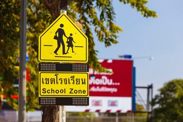 Close-up of yellow school zone warning sign at city street against blurred background, Thailand