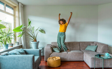 Happy afro american woman dancing on the sofa at home - Smiling girl enjoying day off lying on the couch - Healthy life style, good vibes people and new home concept - 792874060